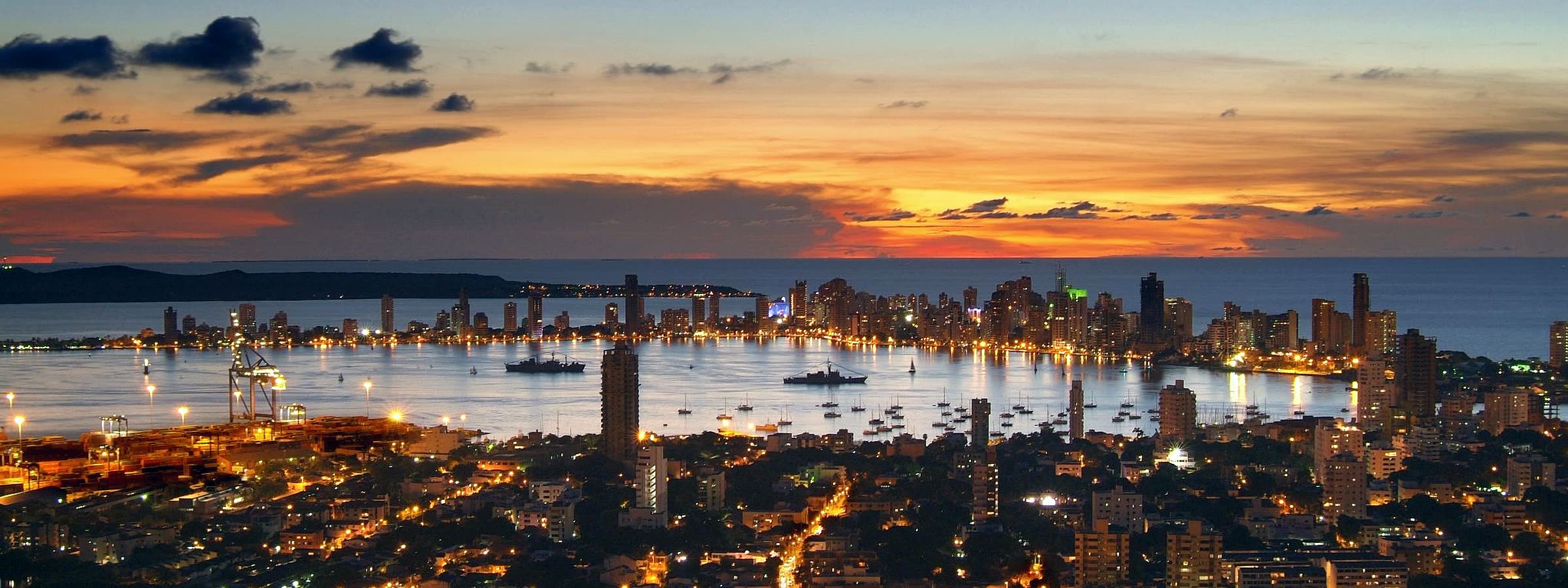 Vista de Cartagena de Indias al atardecer, con la bahía y la zona portuaria iluminada.