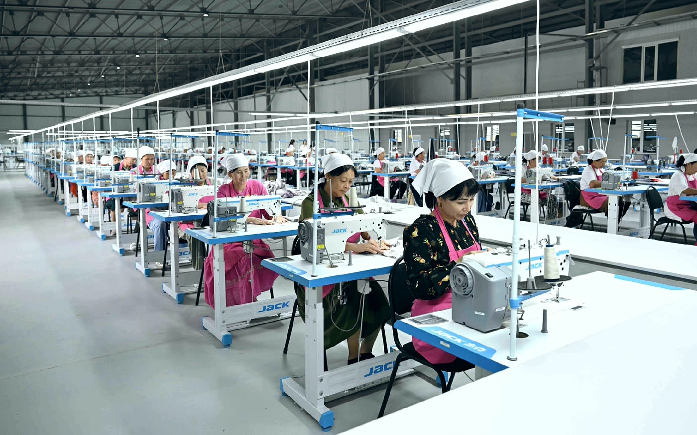 Operarias en un taller de confección industrial trabajando en hileras de máquinas de coser.